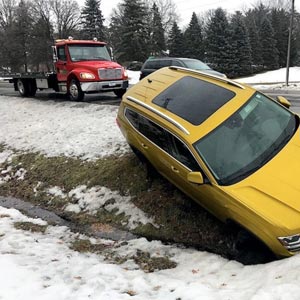 A tow truck with a winch is winching a car out of a ditch pm a snowy day in Wooster, Ohio
