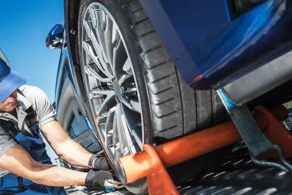A tow truck driver technician prepares a wheel lift towing bar under the front wheels of a car